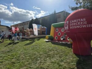 Na zdjęciu widzimy namioty z smakołykami dmuchane atrakcje oraz baner reklamowy Caritas