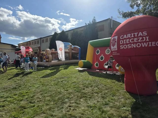 Na zdjęciu widzimy namioty z smakołykami dmuchane atrakcje oraz baner reklamowy Caritas