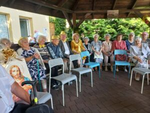 Na zdjęciu widzimy siedzących w altance ogrodowej mieszkańców domu seniora
