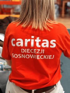 Na zdjęciu widzimy kobietę obróconą tyłem w koszulce Caritas